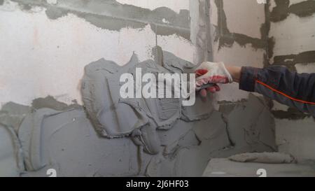 Putting putty on a concrete wall. Construction worker puts a gypsum on the wall with a spatula. Stock Photo