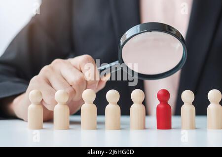 Businesswoman hand holding magnifying glass for recruiting leader man wooden from crowd of employees.Human resource management, Recruitment, Teamwork, Stock Photo