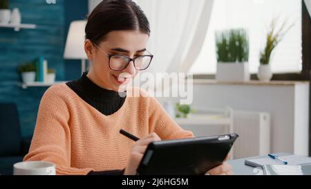 Young adult using digital tablet with stylus to do remote school work, learning assignment knowledge at home. Student working on device for online class lesson, dping research and taking notes. Stock Photo
