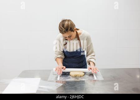 Cook stretching dough with rolling pin in pastry kitchen Stock Photo