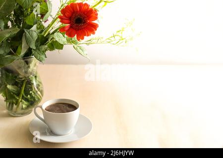 Coffee cup and a flower bouquet in a glass vase on a light wooden table, large copy space, selected focus, narrow depth of field Stock Photo