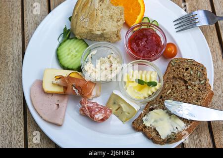 Breakfast or lunch plate with various cold cuts, whole meal bred, jam and fruits on a wooden table in a street cafe, high angle view from above, selec Stock Photo