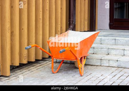 Bright orange wheelbarrow cart for gardening and construction site on the street. Stock Photo