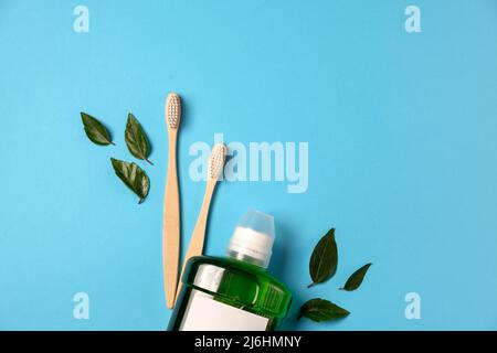 Mouthwash, two wooden bamboo eco friendly toothbrushes, green leaf, isolated on blue color background wall with copy space for advertisement. Teeth hy Stock Photo