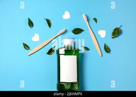 Mouthwash, two wooden bamboo eco friendly toothbrushes, green leaf, white hearts on blue studio background in studio with copy space for advertisement Stock Photo