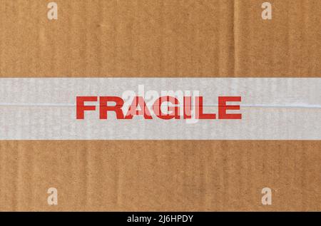 White tape ribbon with the word Fragile in red on cardboard texture Stock Photo