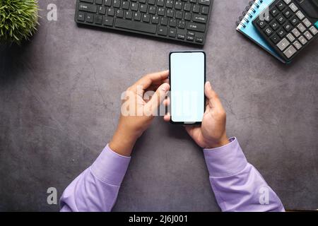 Top view of man hand holding smart phone with empty screen on office desk  Stock Photo