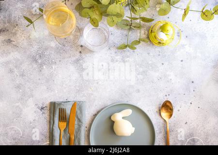 Beautiful Easter table setting in Scandinavian style. Green mint plate with bunny, painted  egg and  cold cutlery on modern concrete background decora Stock Photo
