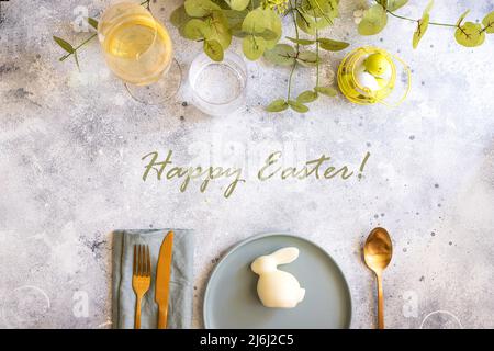 Beautiful Easter table setting in Scandinavian style. Green mint plate with bunny, painted  egg and  cold cutlery on modern concrete background decora Stock Photo