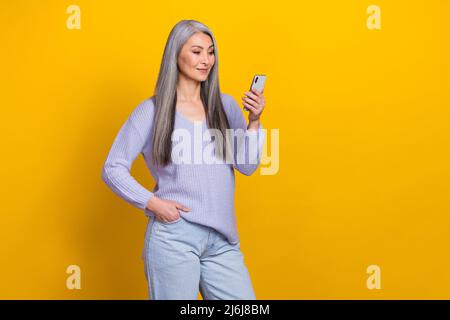 Photo of charming intelligent modern grandma surfing in telephone chatting with friend isolated on yellow color background Stock Photo