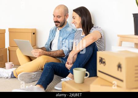 Happy young adult couple using laptop computer in new home Stock Photo