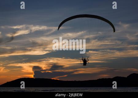 silhouette paramotor or paraglider fly over the sea with beautiful sunset sky background. Stock Photo