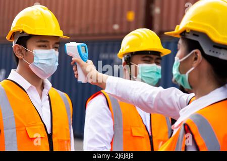 asian man workers wearing face mask checking fever by digital thermometer before entering the work for protecting from covid, covid-19 or coronavirus Stock Photo