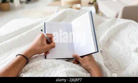 Male Holding Planner In Hands Taking Notes In Bedroom, POV Stock Photo