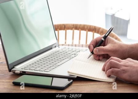 man taking notes on paper while using laptop computer, e-learning or working from home concept Stock Photo
