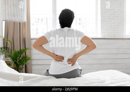 Man suffering from back pain at home in bedroom Stock Photo