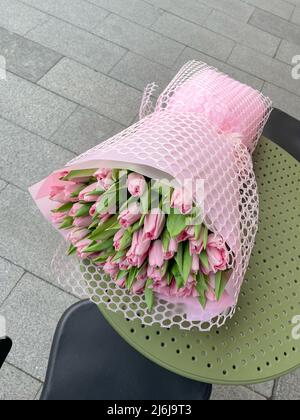 Big Spring bouquet of pink tulipsin pink wrapping laying on cafe table. Stock Photo
