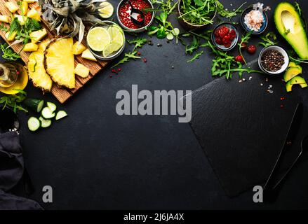 Healthy eating food layout and diet nutrition concept. Pineapple, vegetables, dried fruits, greens and other ingredients for salad preparation on blac Stock Photo