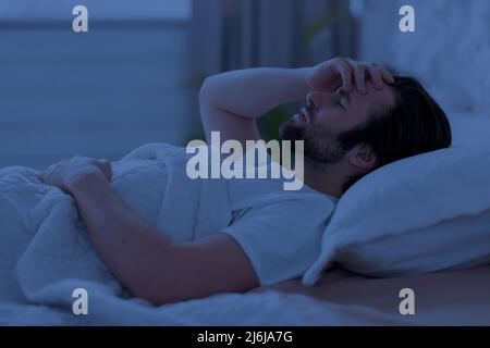 Sleepless man laying in bed alone at night Stock Photo