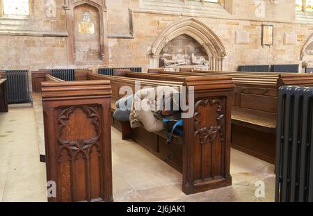 Man sleeping on a wooden pew in Boston cathedral, UK Stock Photo