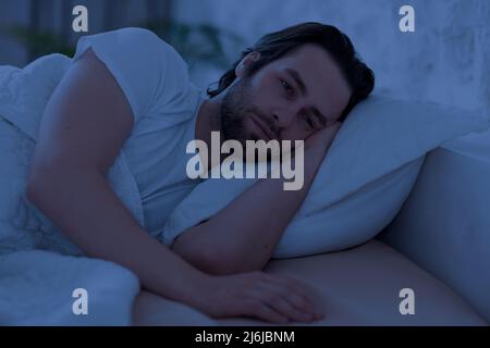 Depressed man cant sleep at night, laying in bed alone Stock Photo