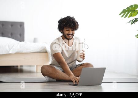 Happy guy sitting on yoga mat with bottle of water Stock Photo