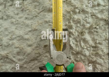 Metal guides for plastering walls, installation of metal beacons on the wall, pliers clamp the beacon holders. Stock Photo