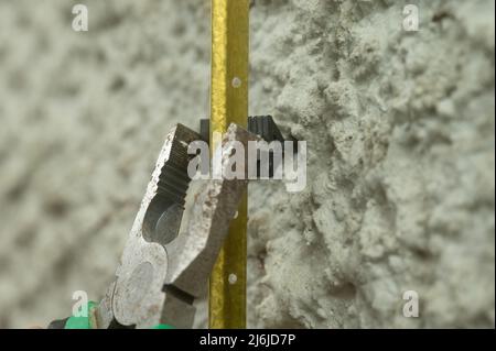Metal guides for plastering walls, installation of metal beacons on the wall, pliers clamp the beacon holders. Stock Photo
