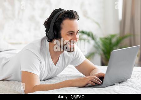 Happy young man laying on bed, using computer Stock Photo