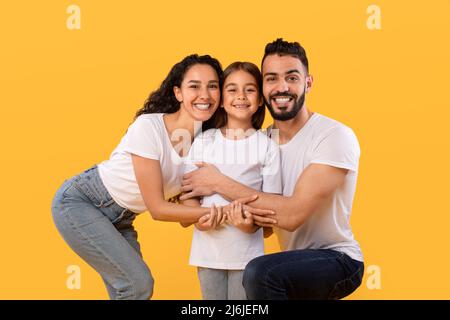 Middle Eastern Parents Embracing Little Daughter Holding Hands, Yellow Background Stock Photo