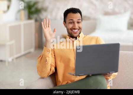 Smiling man working on laptop waving hand Stock Photo