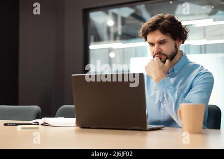 Focused man using laptop sitting at desk in office Stock Photo