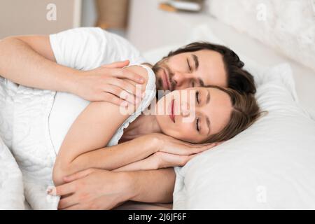 Loving young couple having cozy morning, cuddling together in their sleep on bed Stock Photo