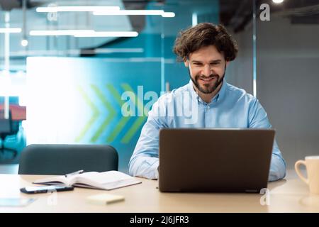 Smiling businessman using laptop sitting at desk in office Stock Photo
