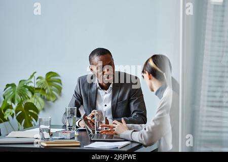 Portrait of young black businessman talking to female colleague during meeting in office against pale blue wall, copy space Stock Photo