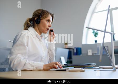 Beautiful female call center operator working on computer in office. Helpline employee Stock Photo