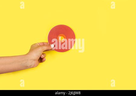 Woman hand holding a red CD on a yellow background with copy space Stock Photo