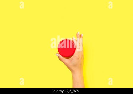 Woman hand holding a red round plastic lid on a yellow background with copy space Stock Photo