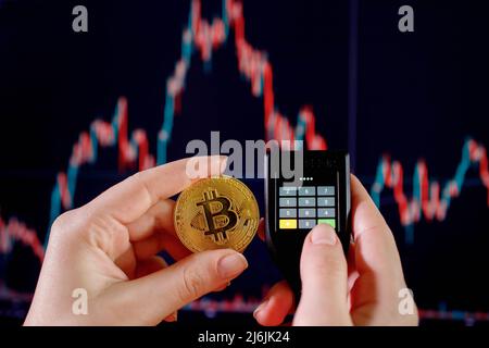 Close up womans hand holding bitcoin and enter the password on cryptocurrencey hardware cold wallet on stock market graph background. Secure cryptocurrency storage. Stock Photo