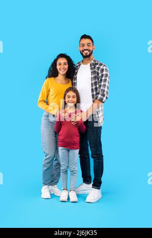 Cheerful Arabic Family Of Three Posing Embracing, Blue Background, Vertical Stock Photo