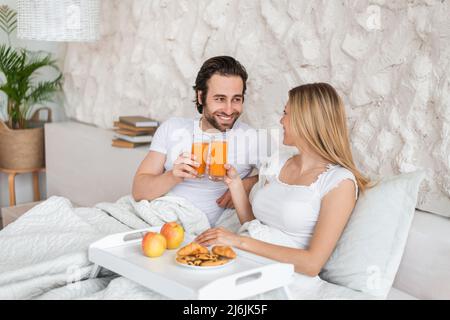 Happy millennial couple having breakfast in bed together, spending honeymoon at hotel, copy space Stock Photo