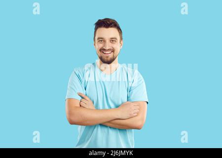 Happy handsome young man in a blue T shirt standing with his arms crossed and smiling Stock Photo
