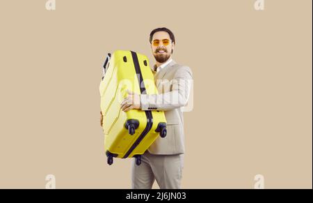 Handsome businessman in suit going on holiday or business trip with his yellow suitcase Stock Photo