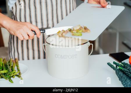 Compost the kitchen waste, recycling. Household woman scraping, throwing vegetables cutting leftovers into the garbage, compost bin while cooking on h Stock Photo