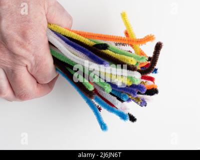 person clutching a bunch of sparkle and neon rainbow pipe cleaners on a white background Stock Photo