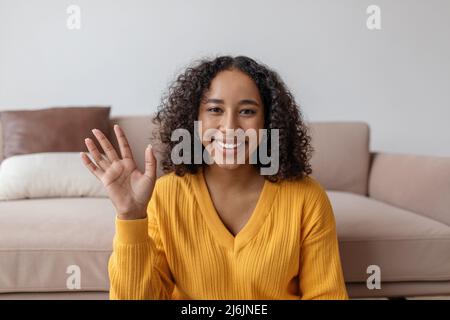 Positive young black woman waving at webcam, talking to family or friend on laptop from home Stock Photo