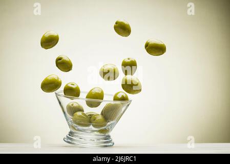 Big green olives jumping out from glass bowl, on colored background Stock Photo