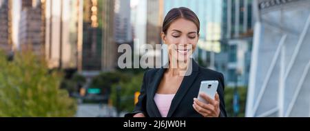 Woman sms texting using app on smart phone in city business district. Young business woman using smartphone smiling happy wearing suit jacket outdoors Stock Photo