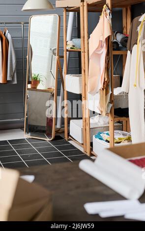 Part of large modern workshop of tailor or fashion designer with mirror in the corner between rack with clothes and shelves with supplies Stock Photo