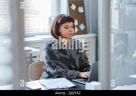 Portrait of young African American woman with short haircut using laptop computer at workplace in office Stock Photo